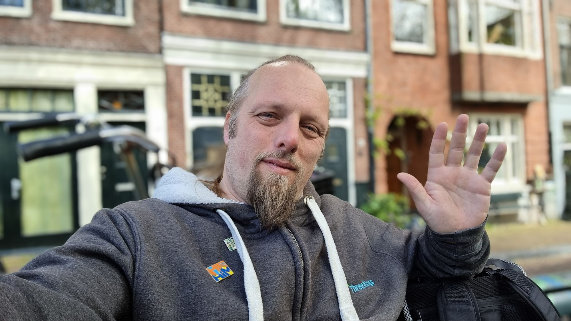 Full image of Dan, sat on a bench in Amsterdam, waves.