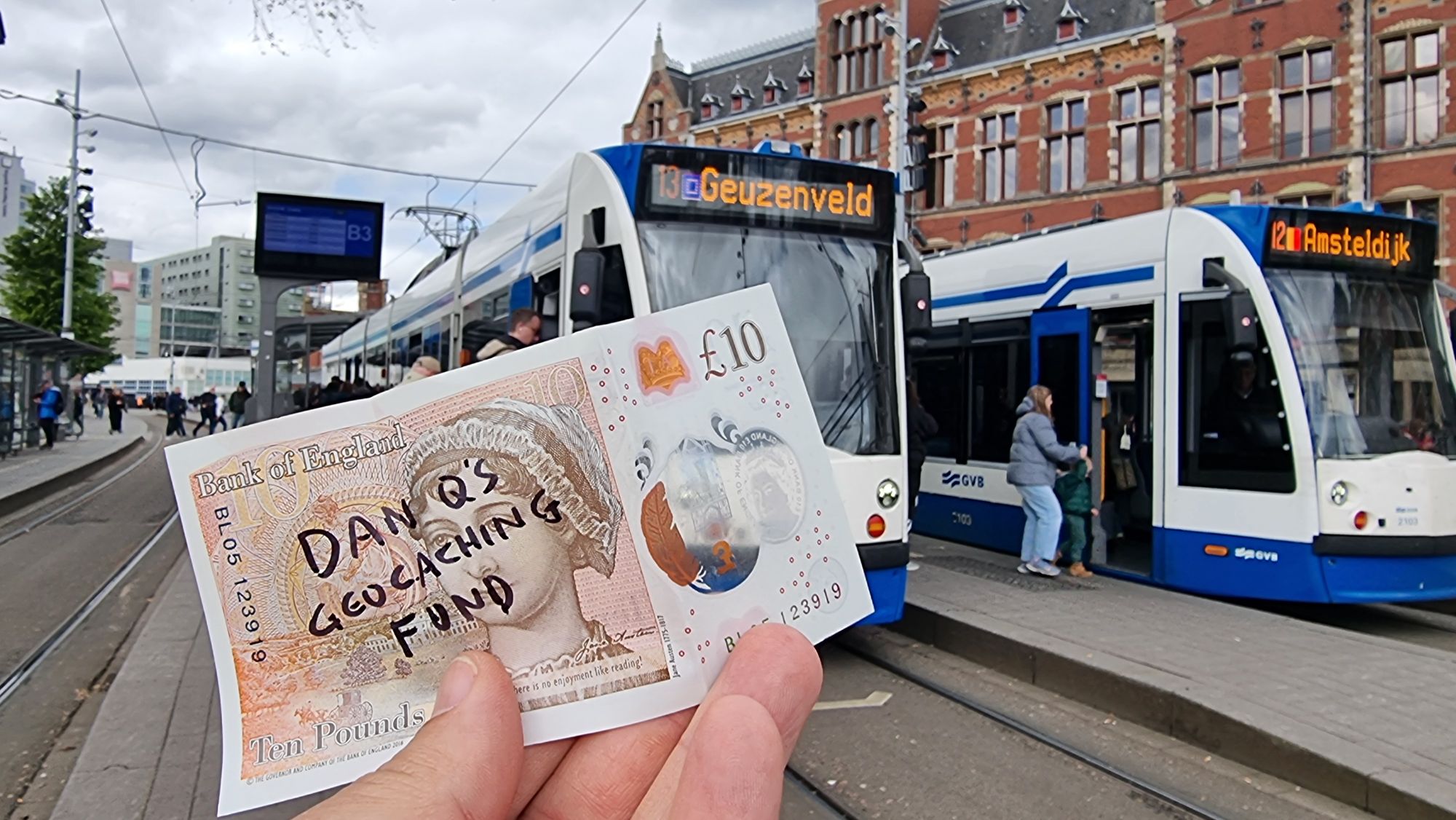 Full image of A £10 note with "Dan Q's Geocaching Fund" written on it in front of a number 13 tram.