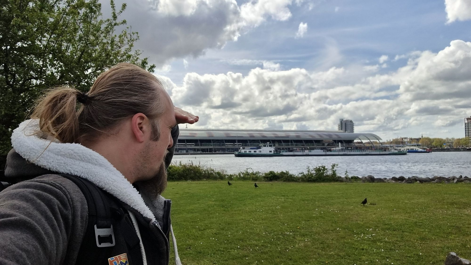 Full image of Dan puts his hand to his brow as he looks out to sea near Amsterdam.