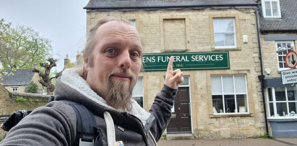 Dan points to a bricked-up first storey window on a stone building used by a funeral services company.
