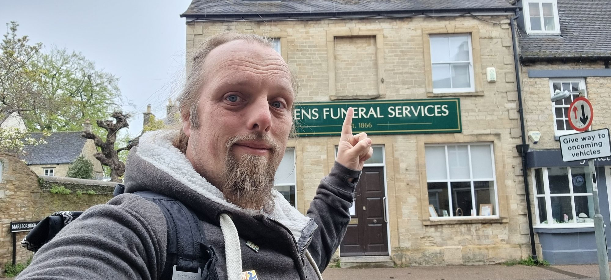 Full image of Dan points to a bricked-up first storey window on a stone building used by a funeral services company.