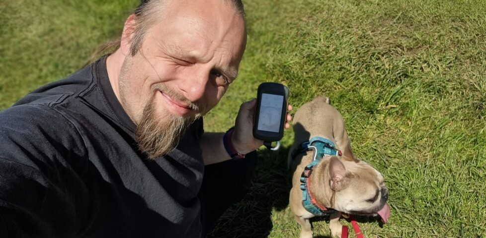 Dan squints into the sunlight in a grassy field, alongside a dog.