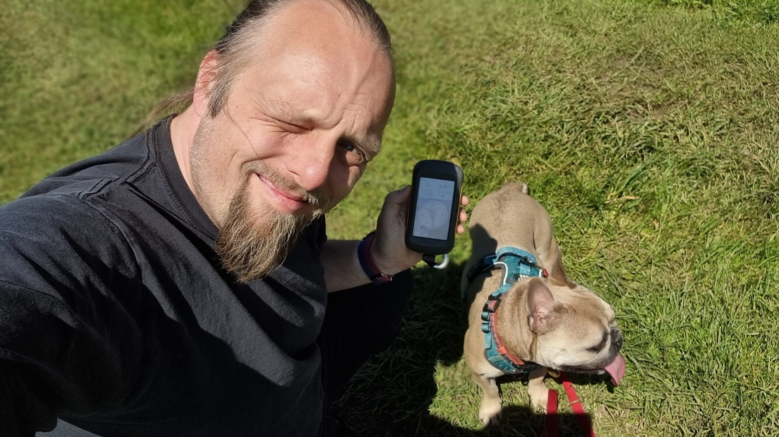 Full image of Dan squints into the sunlight in a grassy field, alongside a dog.