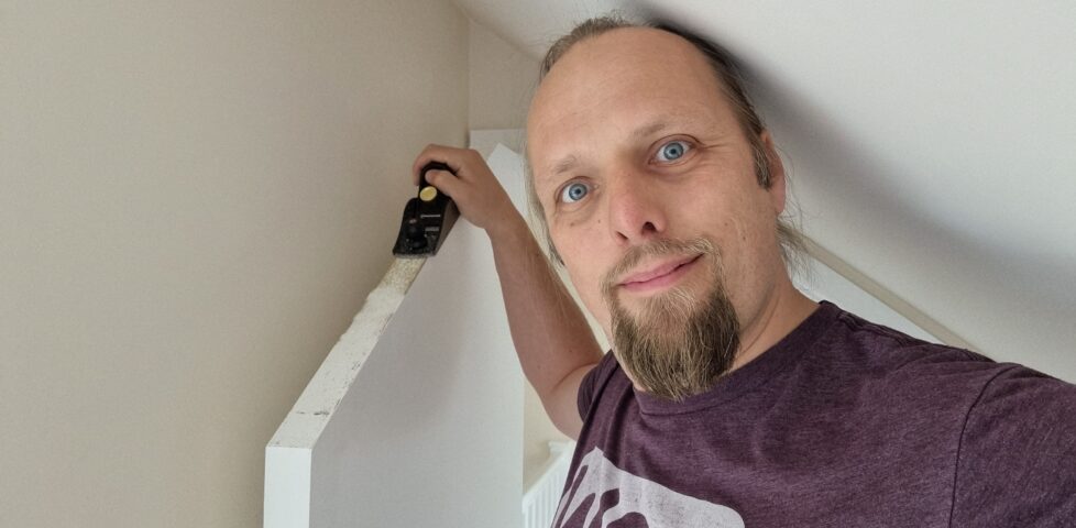 Dan stands alongside a door, his hand on top of a plane, itself on top of the door.