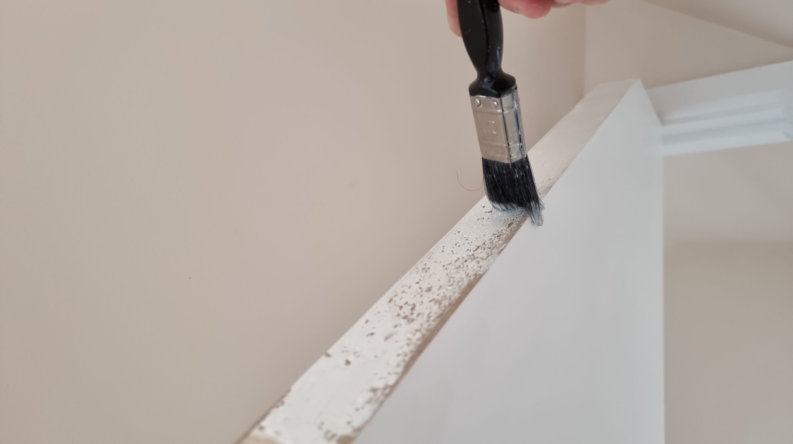 Full image of A paintbrush applies white paint to the top of a door.