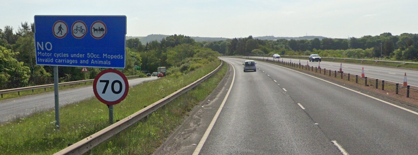 Full image of Google Street View photo from the A1 East of Edinburgh, showing a blue "No motor cycles under 50cc, moped,s invalid carriages and animals" sign alongside a 70mph sign.