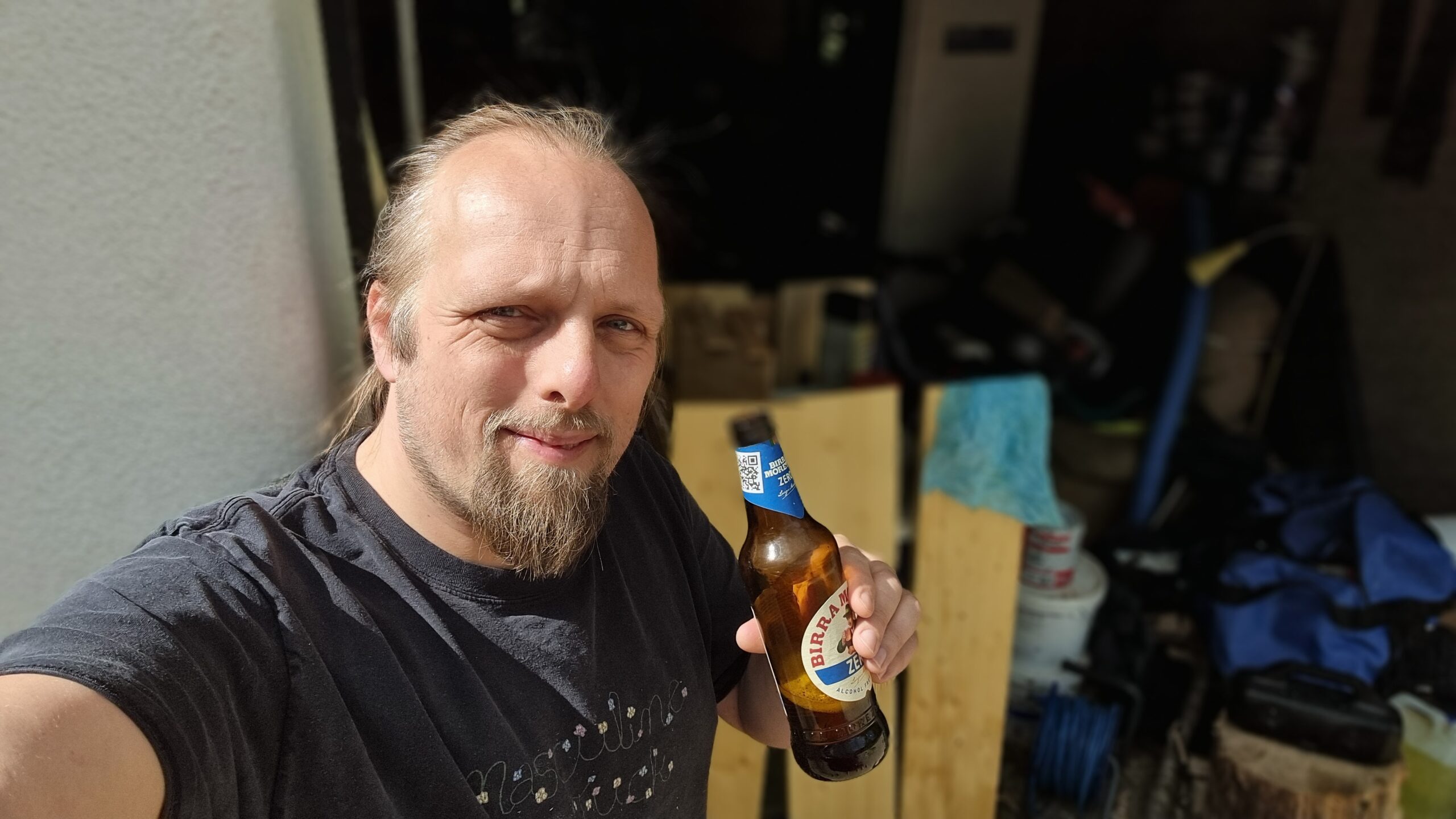 Full image of Dan drinks a 0% alcohol beer in front of three upright planks of wood.