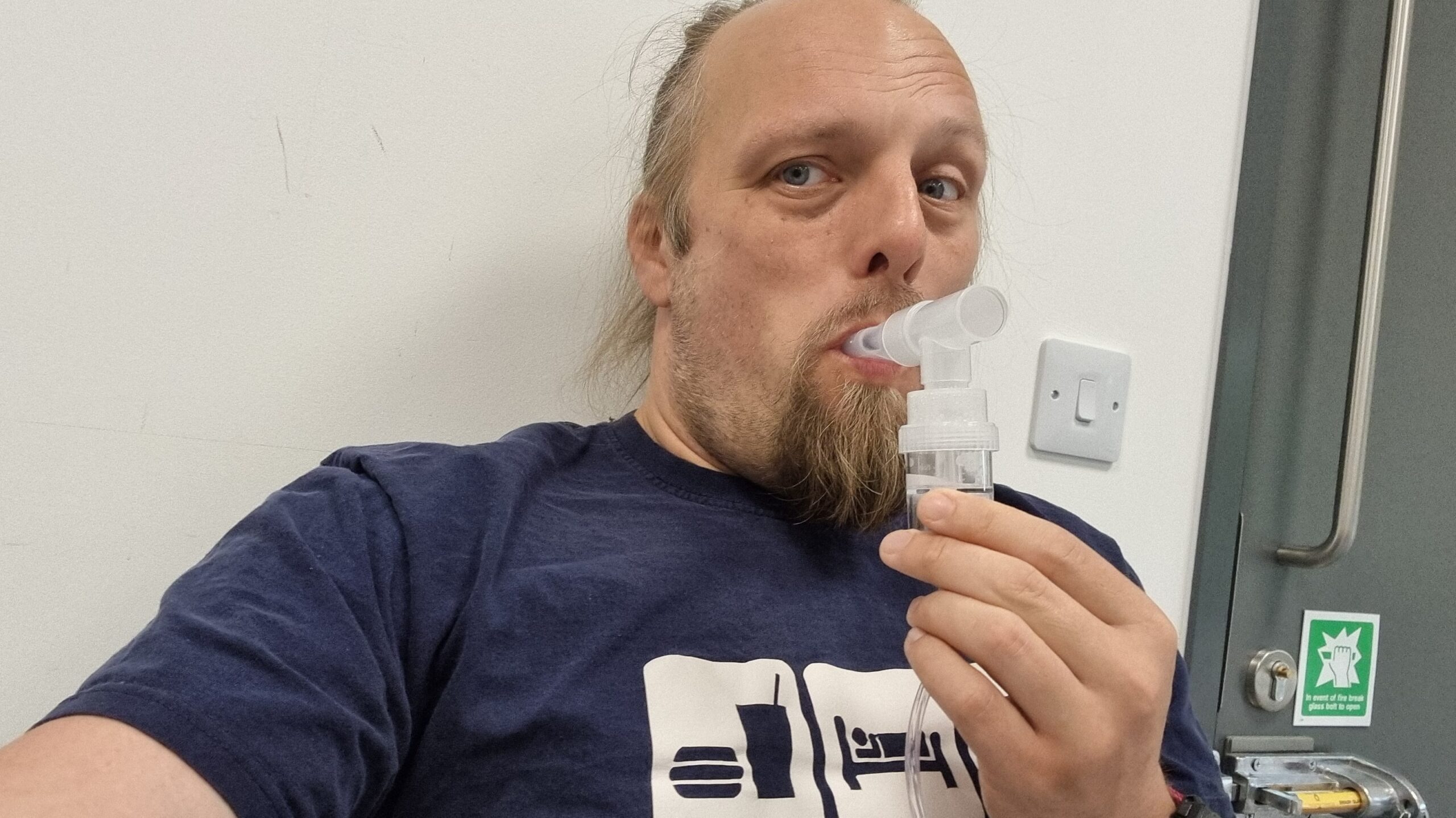 Full image of Dan holds a piece of medical apparatus to his mouth.