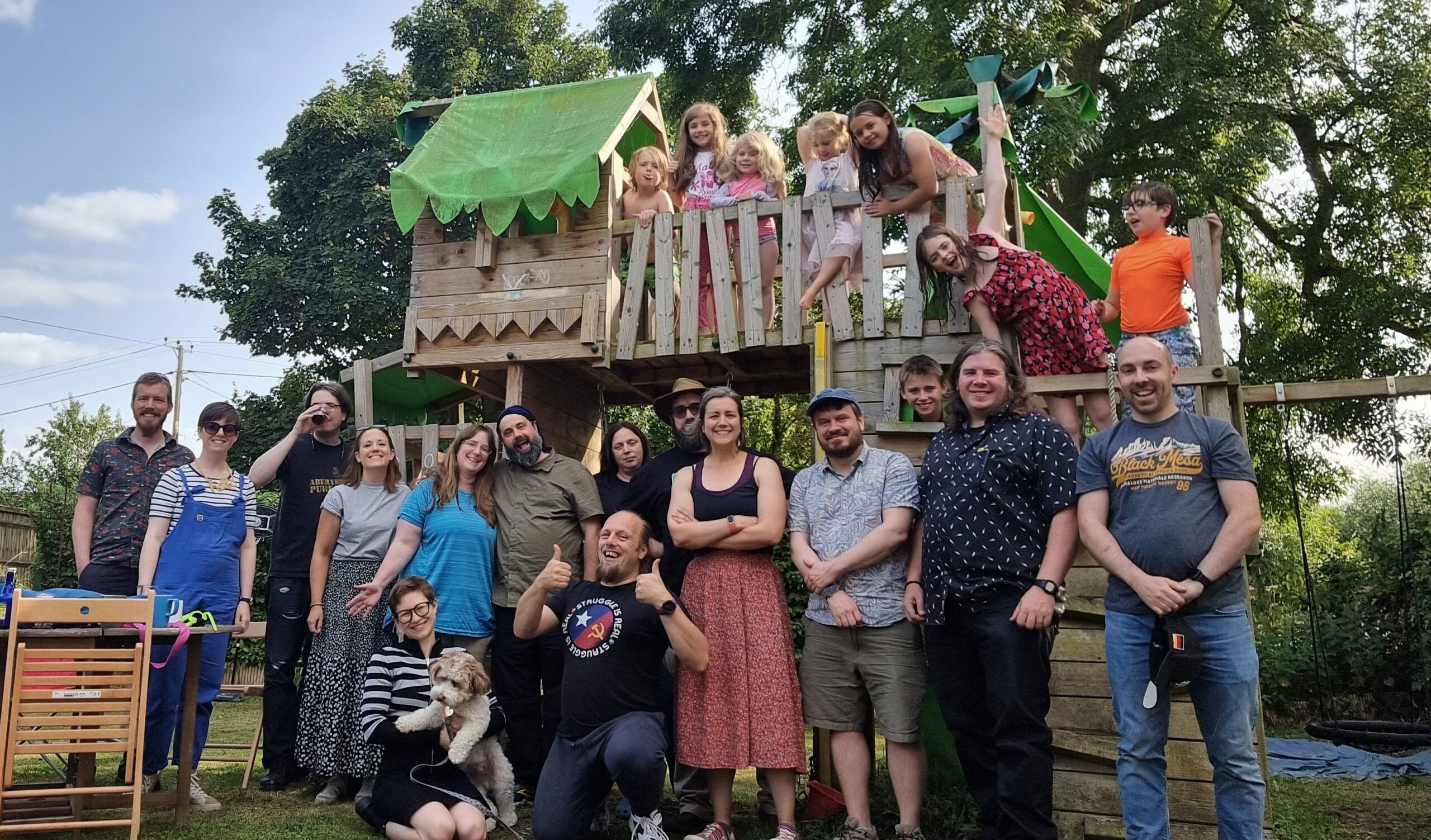 Full image of 14 adults, 8 children, and a dog stand on/in front of a garden climbing frame: Dan is in the centre.
