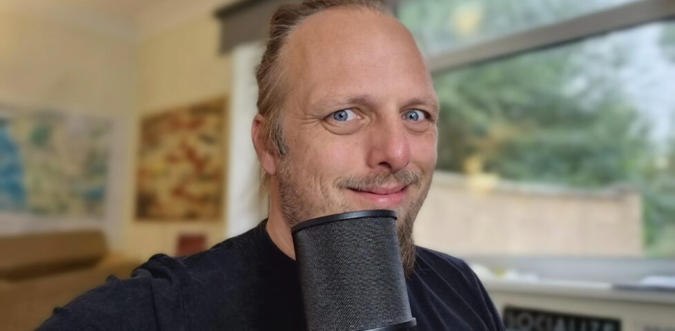 Dan, a microphone in front of him, smiles at the camera.