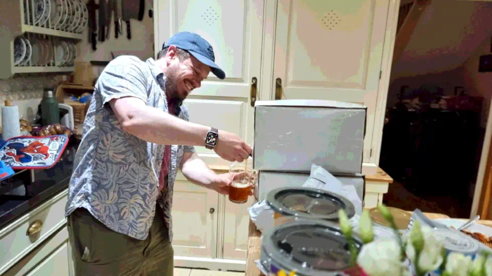 Full image of A man wearing a cap pours himself a beer from a 10-litre box, reduced to a "Web safe" palette.