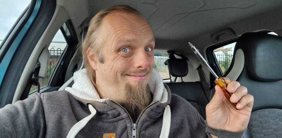 Dan, sitting in a car, holding a screwdriver and smiling.