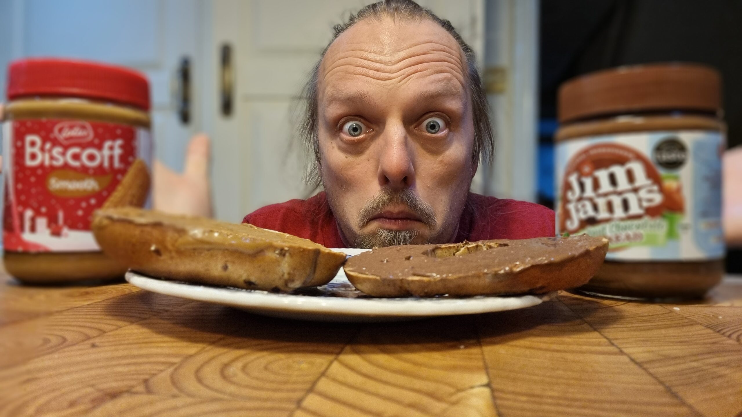 Full image of Dan, looking confused, next to a cinnamon and raisin bagel with JimJams on one half and Biscoff on the other half (and their respective jars).