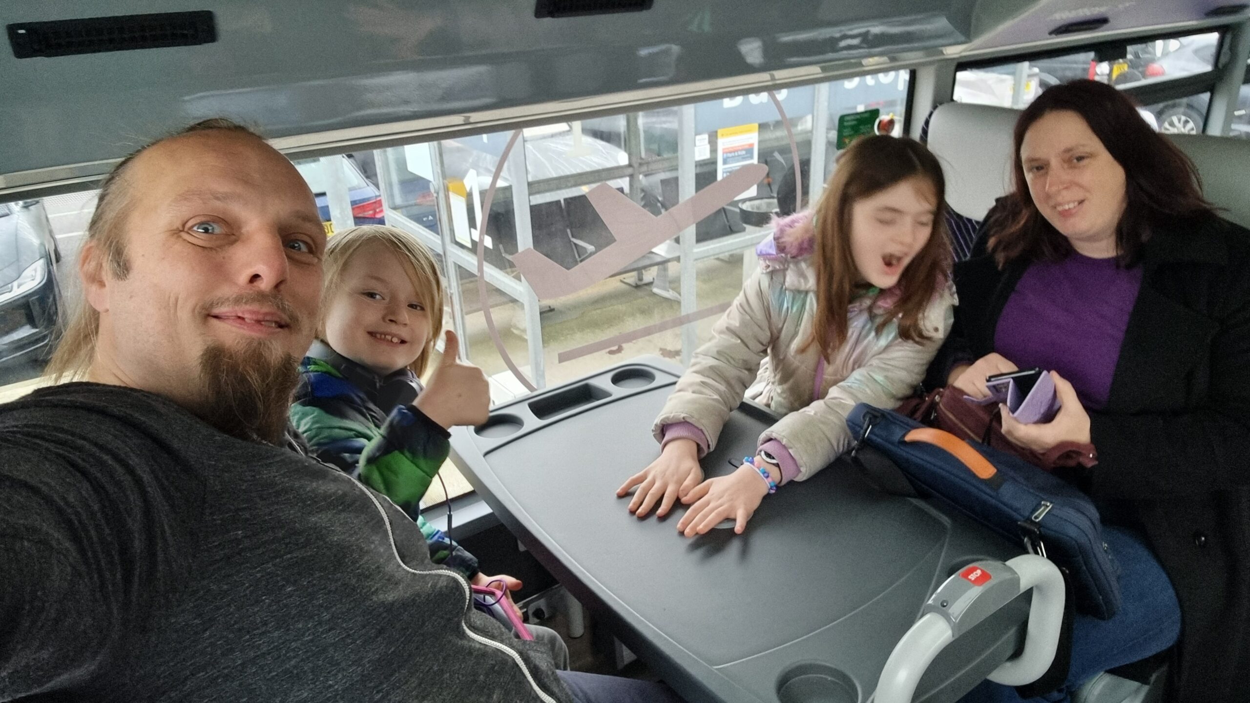 Full image of Dan, Ruth, and their children on an airport car park shuttle bus.