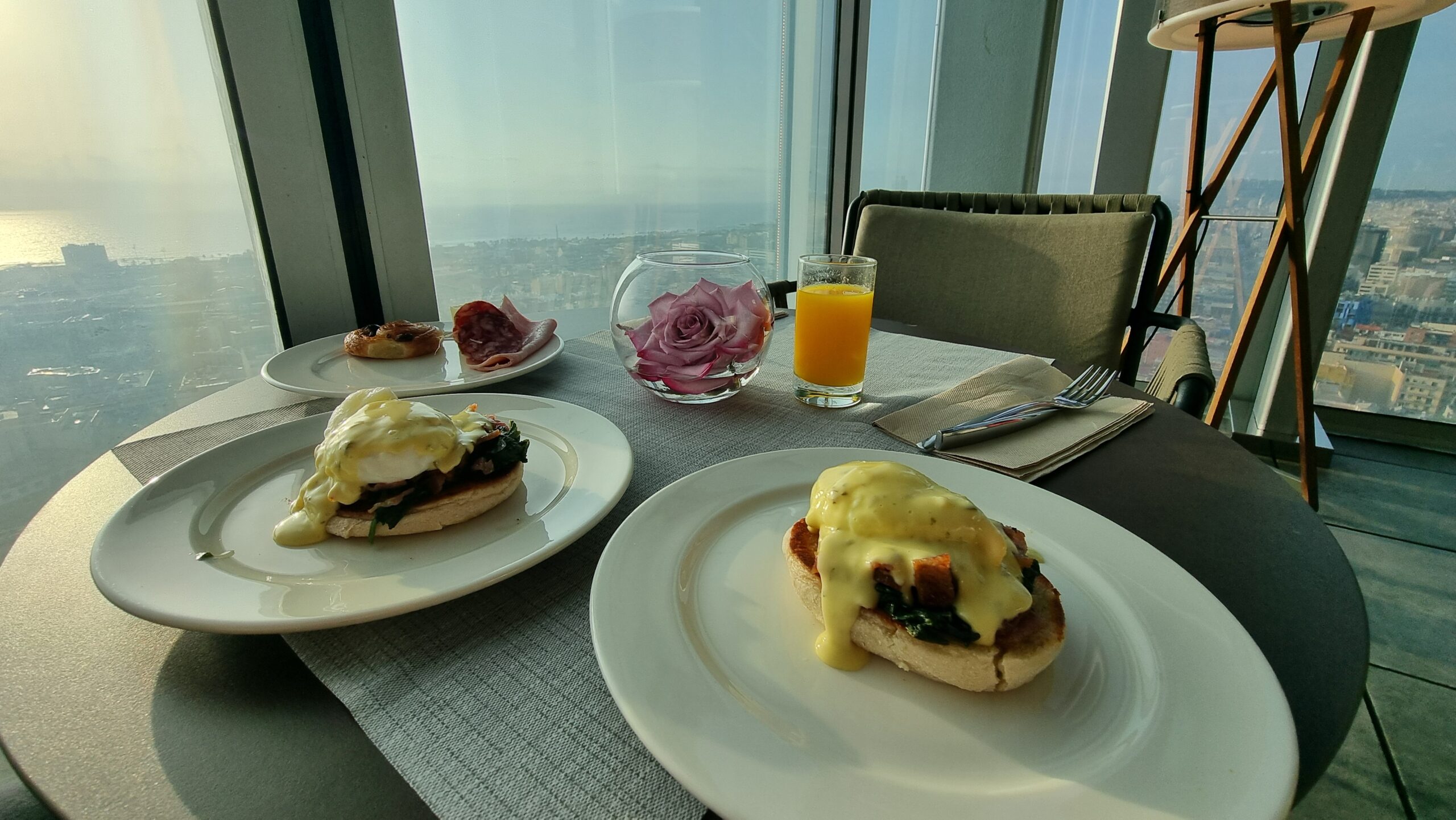 Full image of Two portions of eggs benedict, in front of a window showing a 25th-storey view of Barcelona.