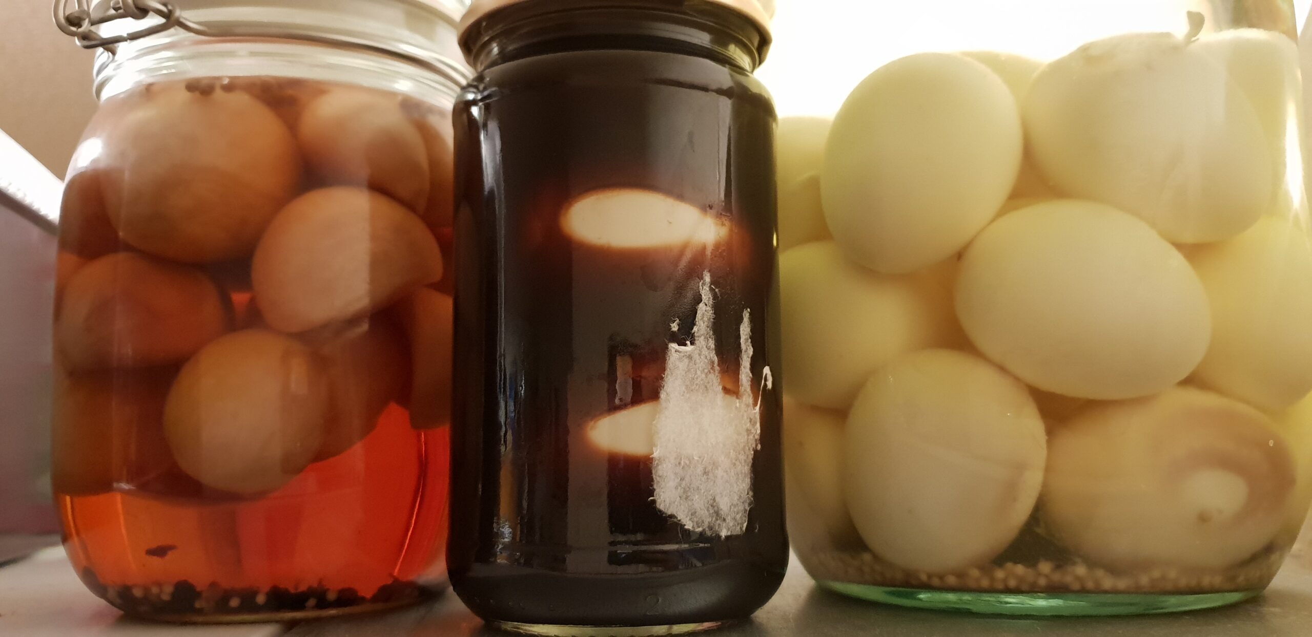 Full image of Three jars of homemade pickled eggs; one in each of a chilli-spiced vinegar, balsamic vinegar, and white vinegar.