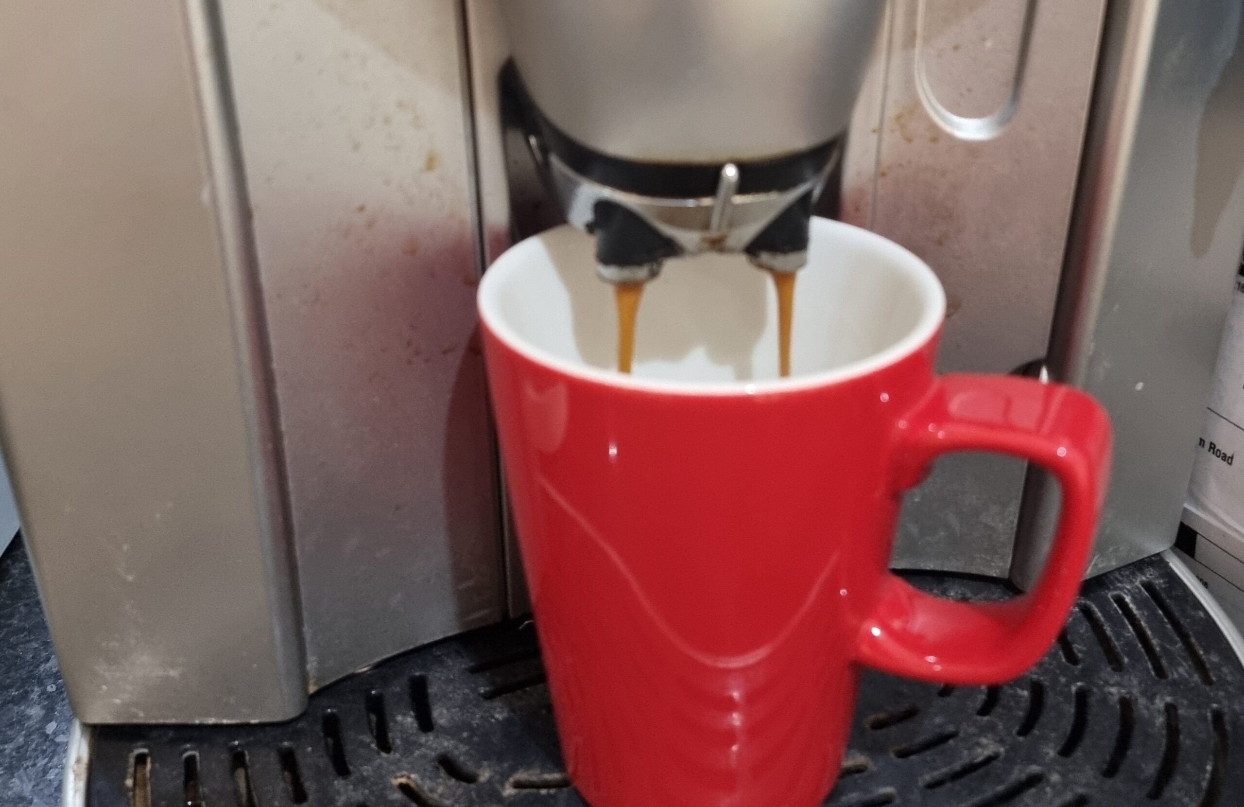 Full image of A red mug being filled by a coffee machine.