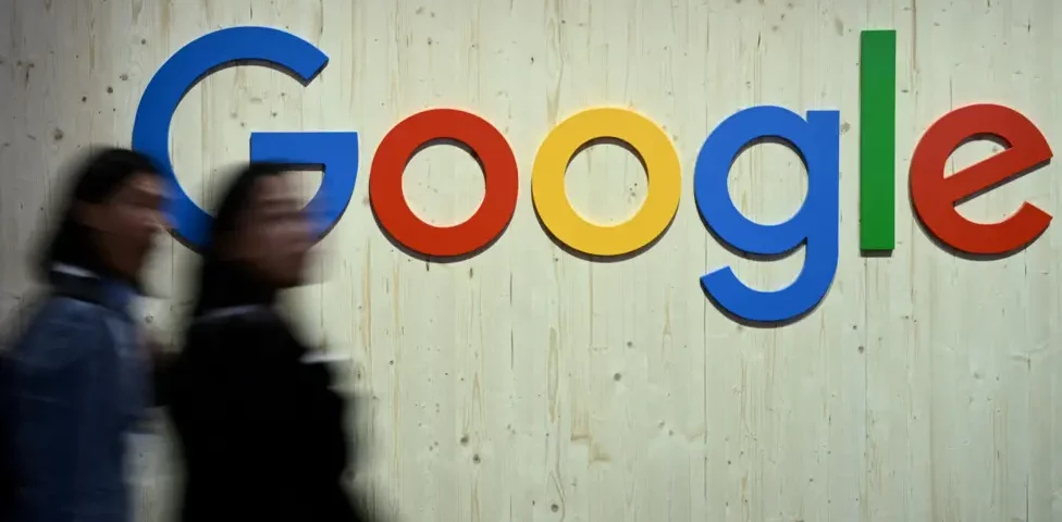 People walk in front of a Google logo.