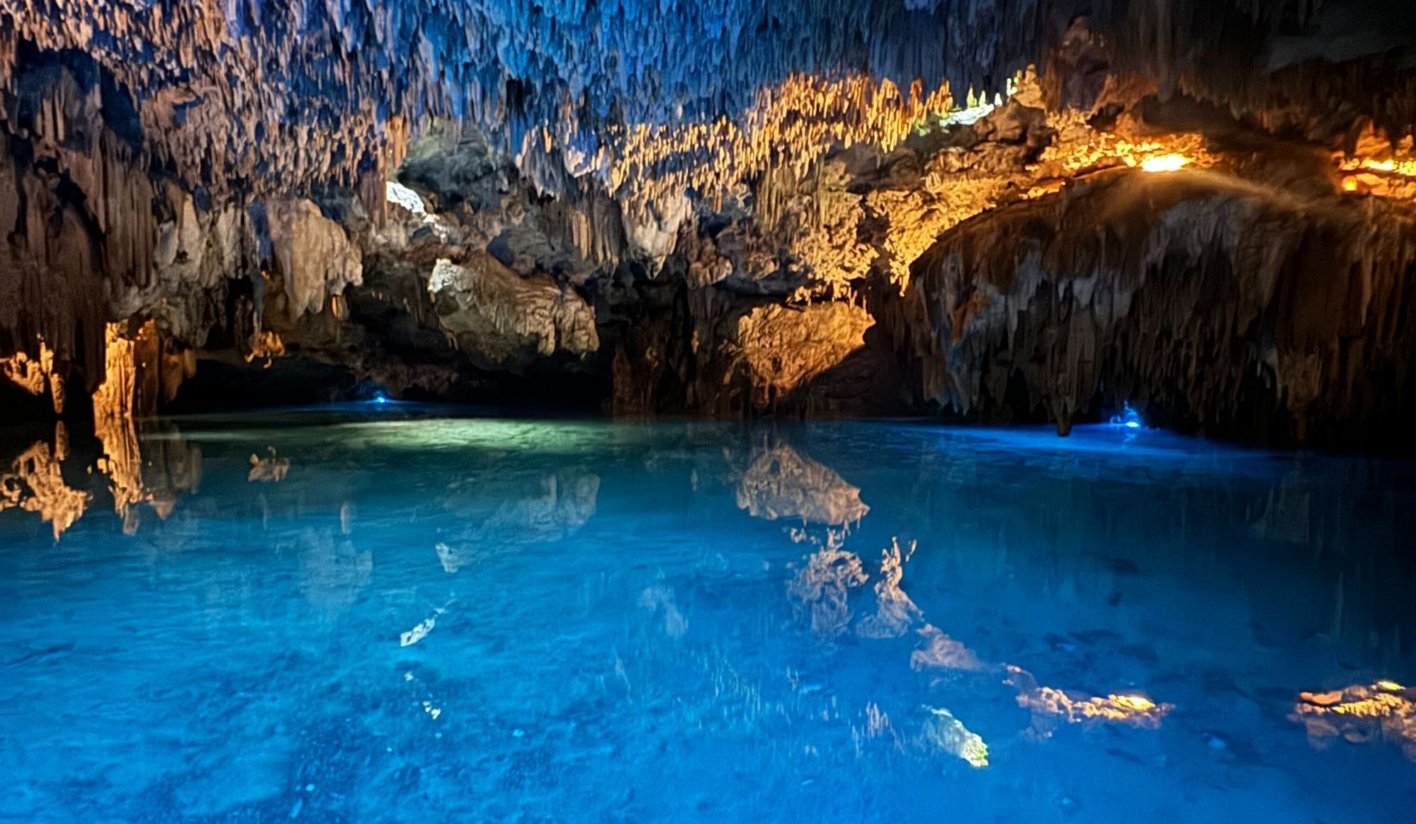 Full image of Stalactite-strewn cave deeply filled with clear blue water.