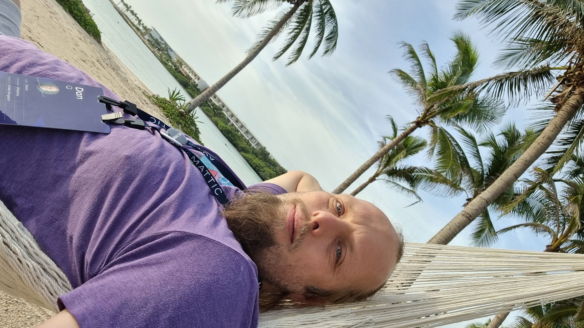 Full image of Dan lies in a hammock under a warm sun, smiling.