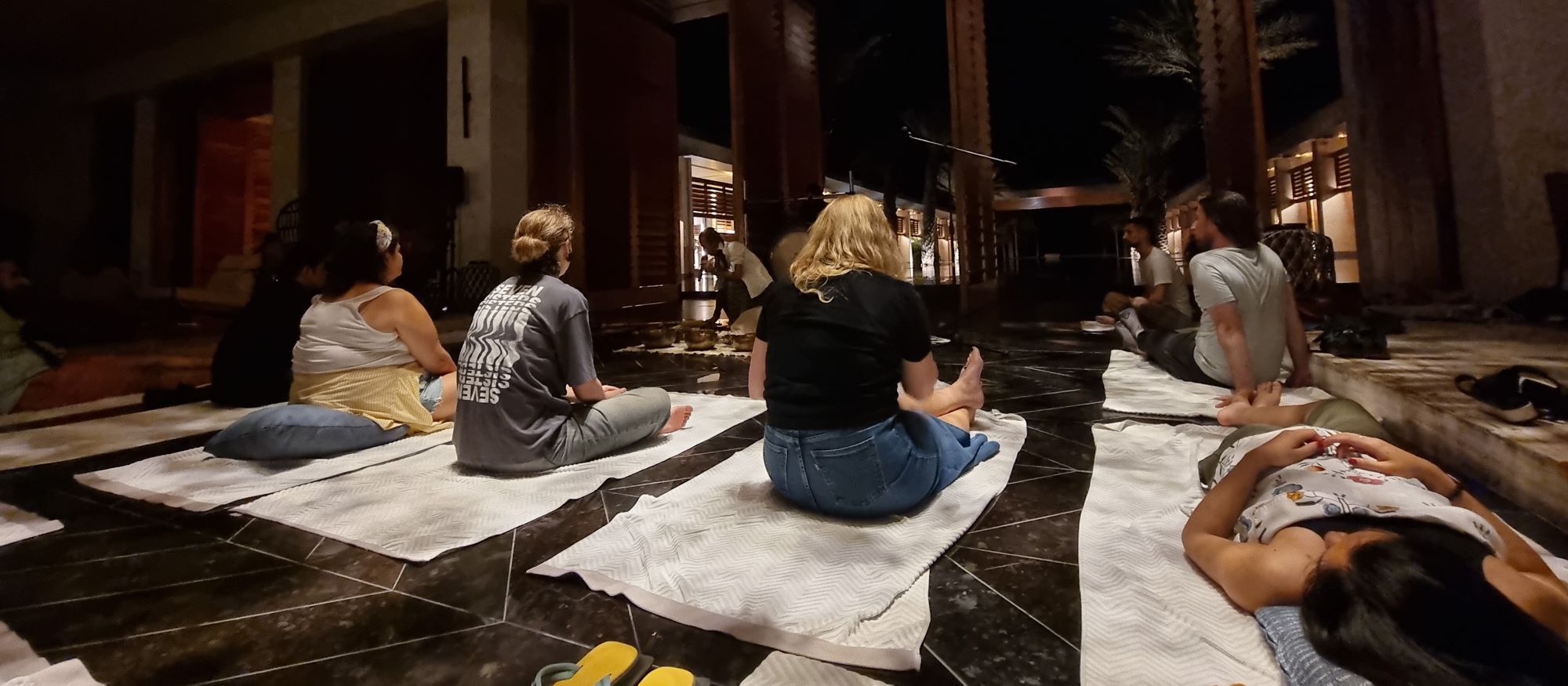 Full image of A group of people lie or sit cross-legged on towels in front of a collection of musical instruments.