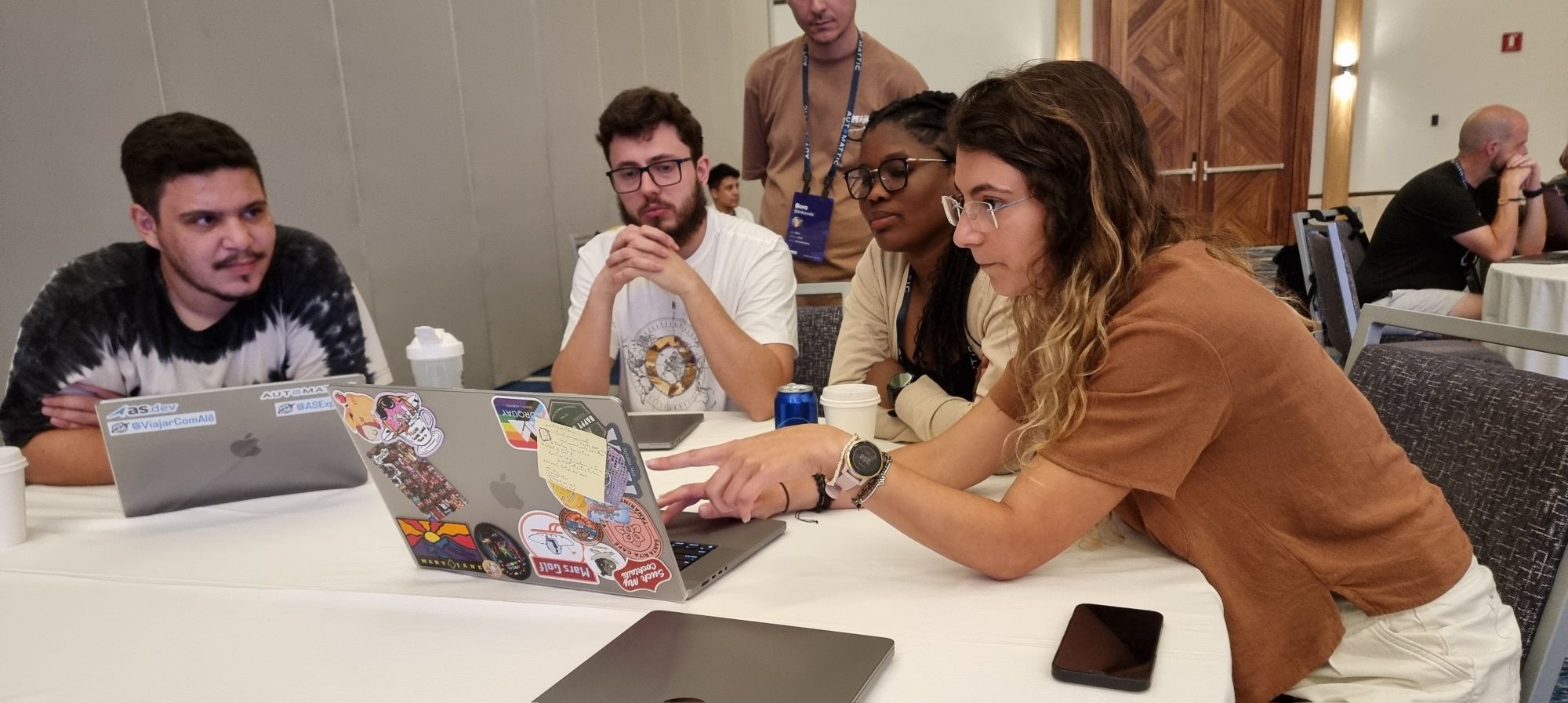 Full image of Two men and two women sit around a sticker-covered Macbook laptop, collectively looking at its screen.