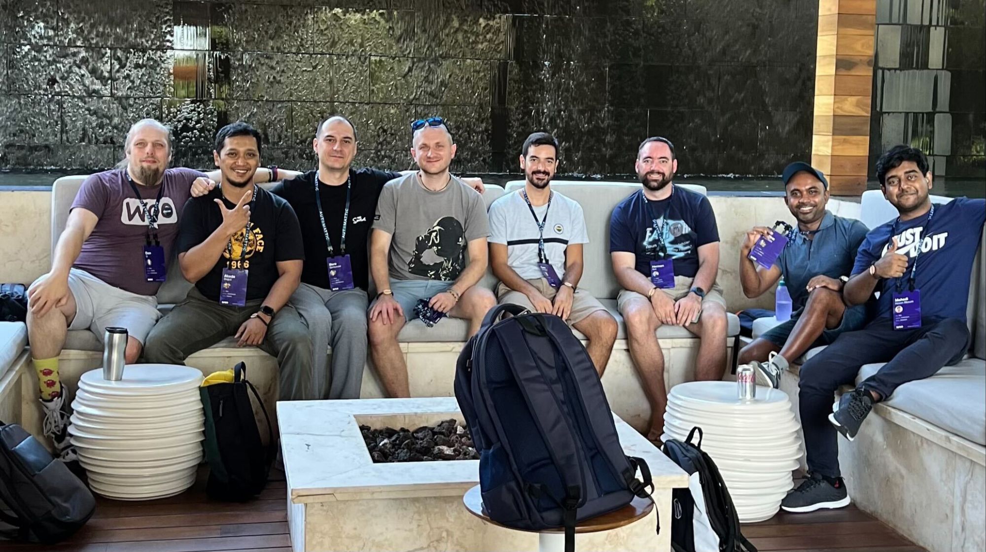 Full image of Dan sits with seven other men in an ourdoor bar area, with water trickling down an ornamental wall behind them.