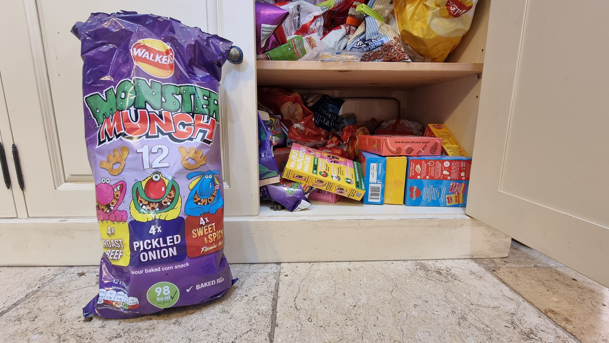 Full image of Snack cupboard next to a 12-pack of Monster Munch featuring three flavours: Roast Beef, Flamin' Hot, and Pickled Onion.