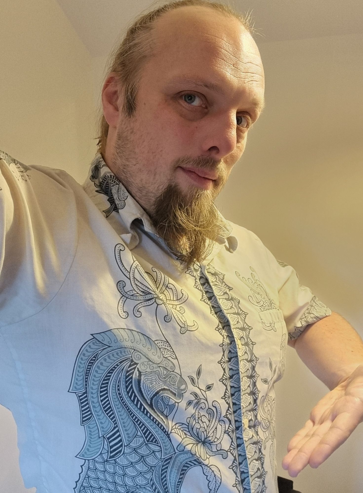 Full image of Dan wearing an off-white shirt decorated with intricate inky designs reminiscent of dragons.