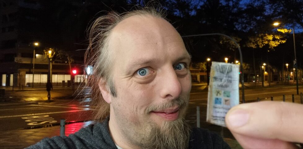 Dan, on a pre-dawn city street, smugly shows the front cover of a little-finger-sized geocaching logbook.
