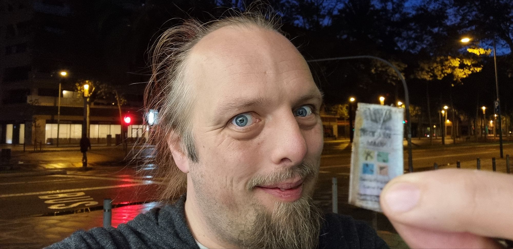 Full image of Dan, on a pre-dawn city street, smugly shows the front cover of a little-finger-sized geocaching logbook.