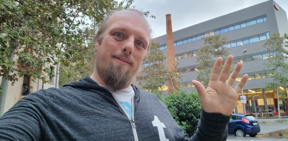 Dan waves in front of an old brick chimney surrounded by modern office and retail buildings.