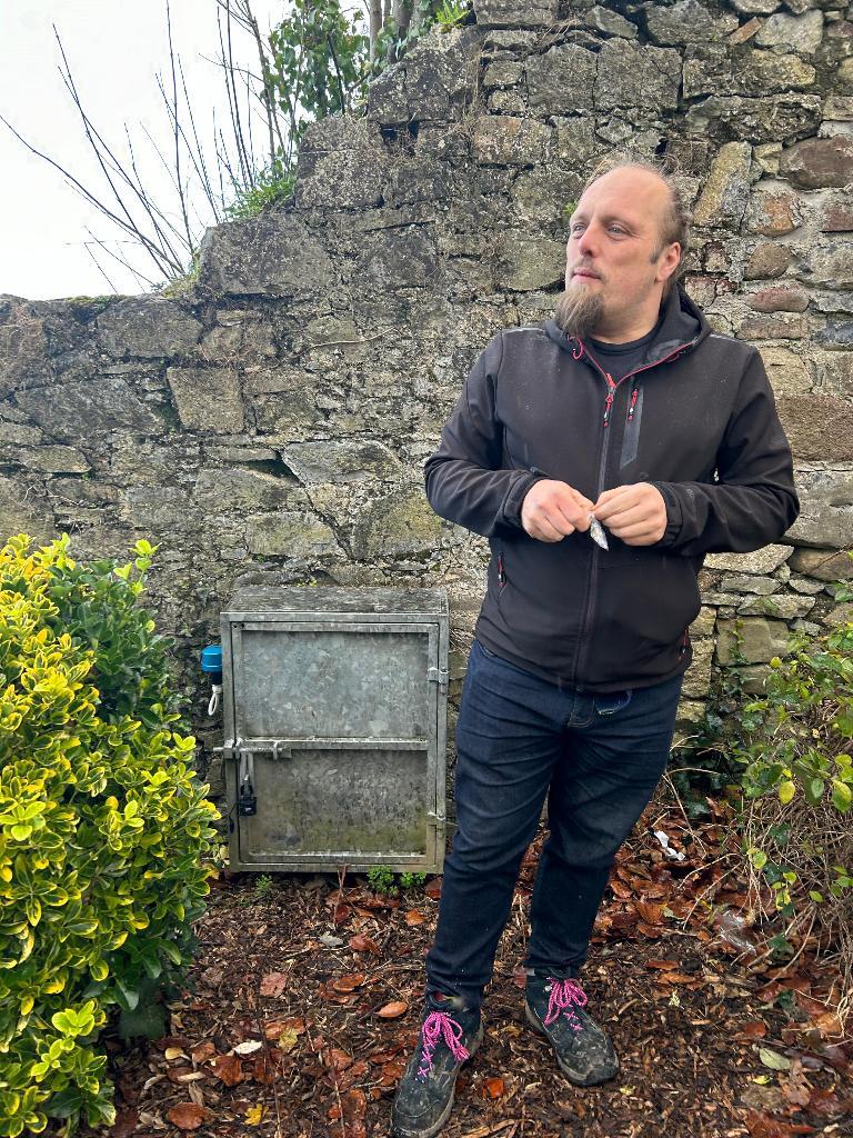 Full image of Dan unrolls a cache log while standing in a flowerbed.