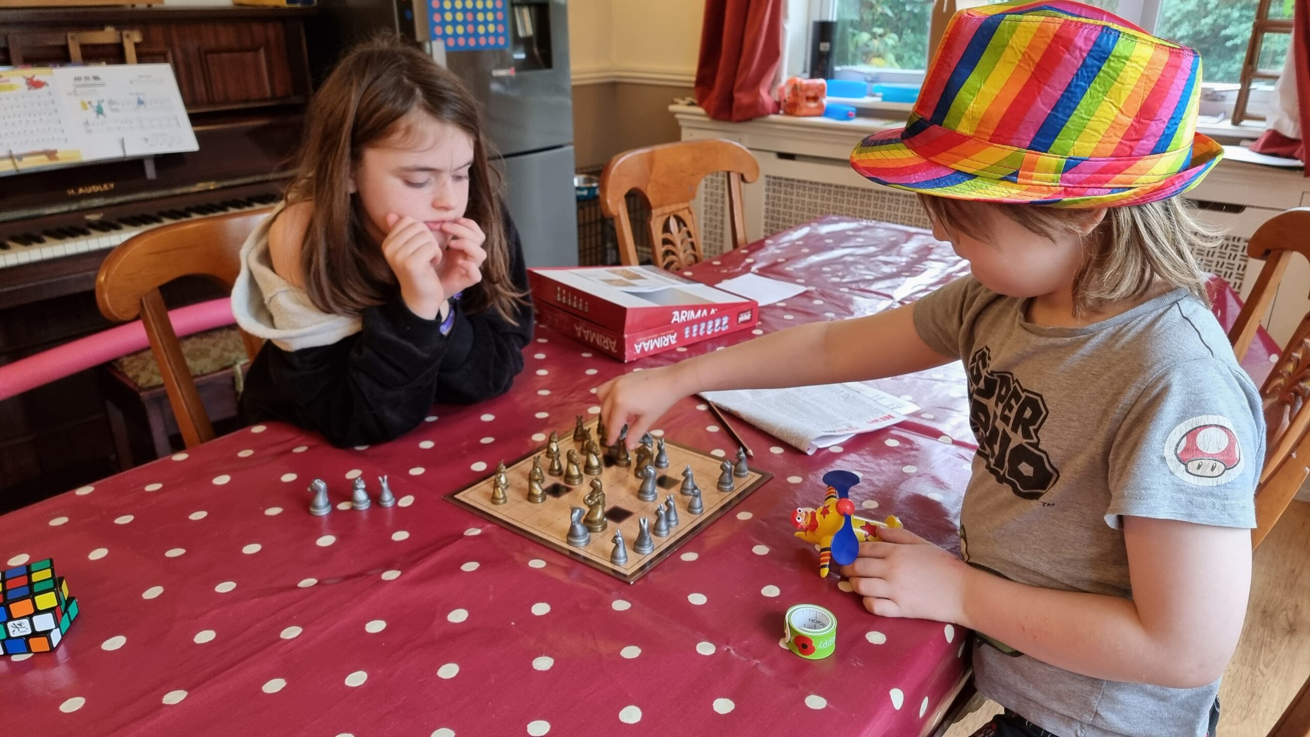 Full image of In a cluttered dining room, two children play Arimaa, a chess-like board game.