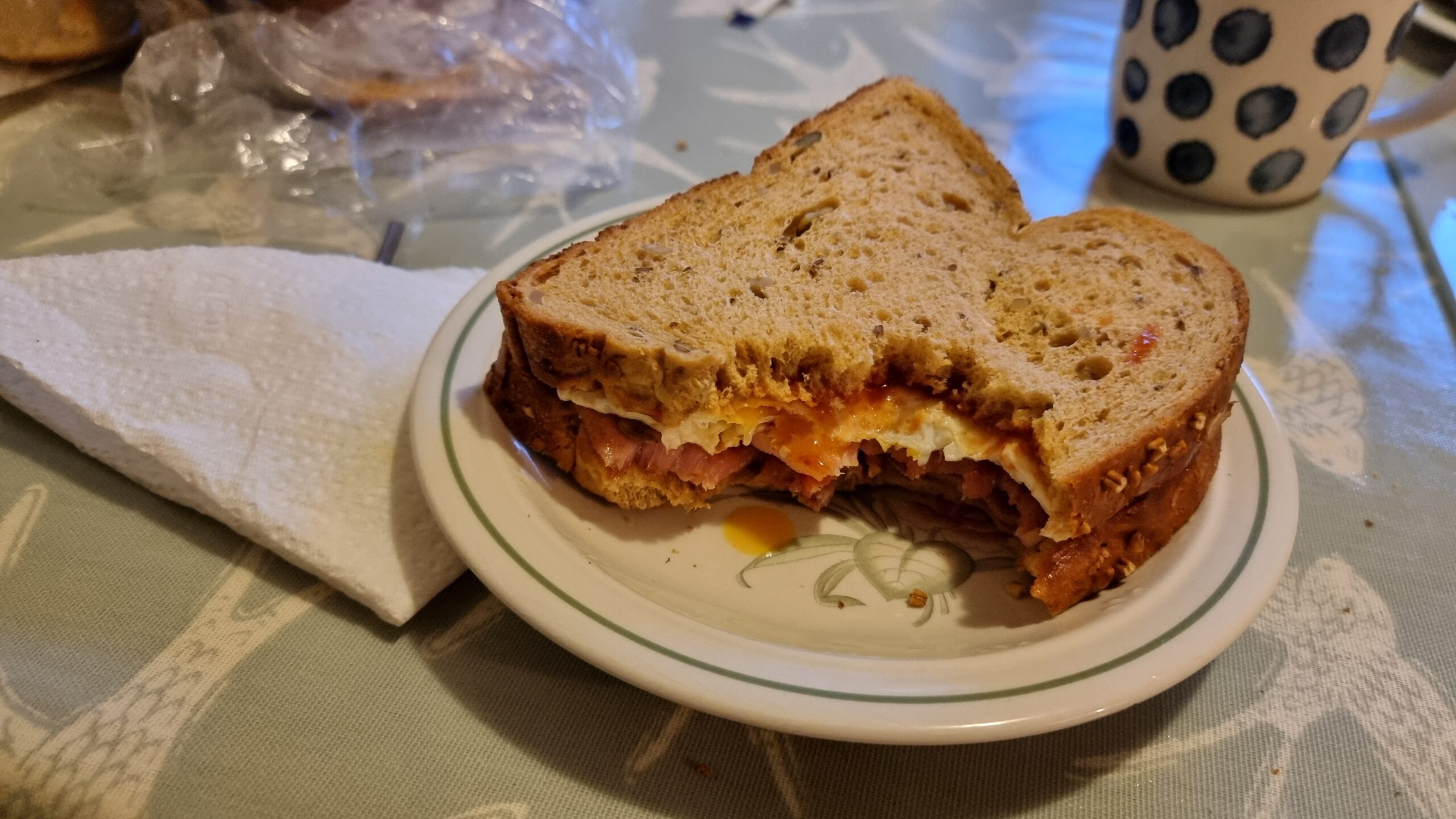 Full image of Bacon and egg sandwich on granary bread, with two bites taken out of it.