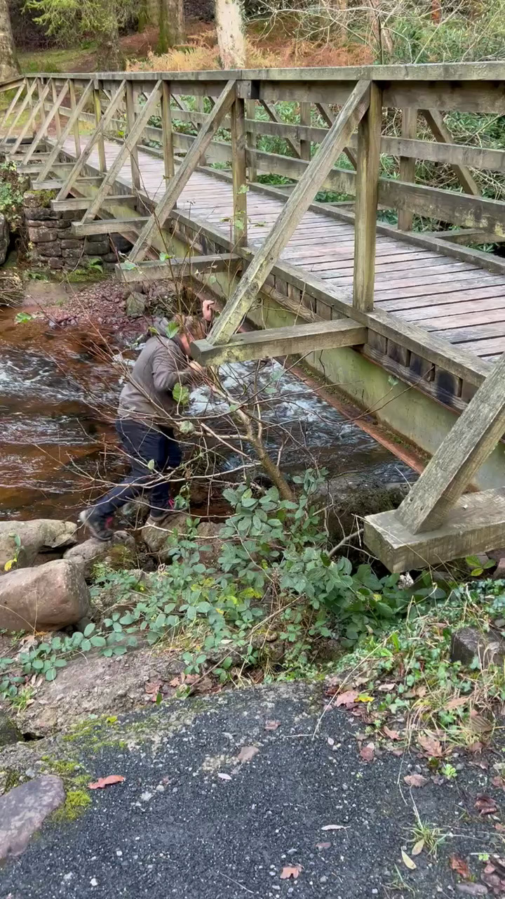 Full image of Dan clambers under a wooden bridge over a river.