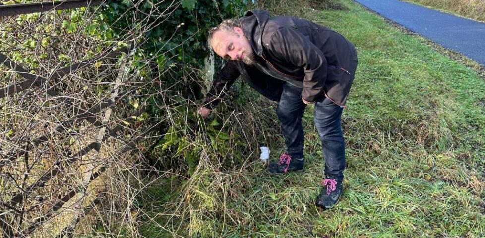 Dan reaches behind a fence post.