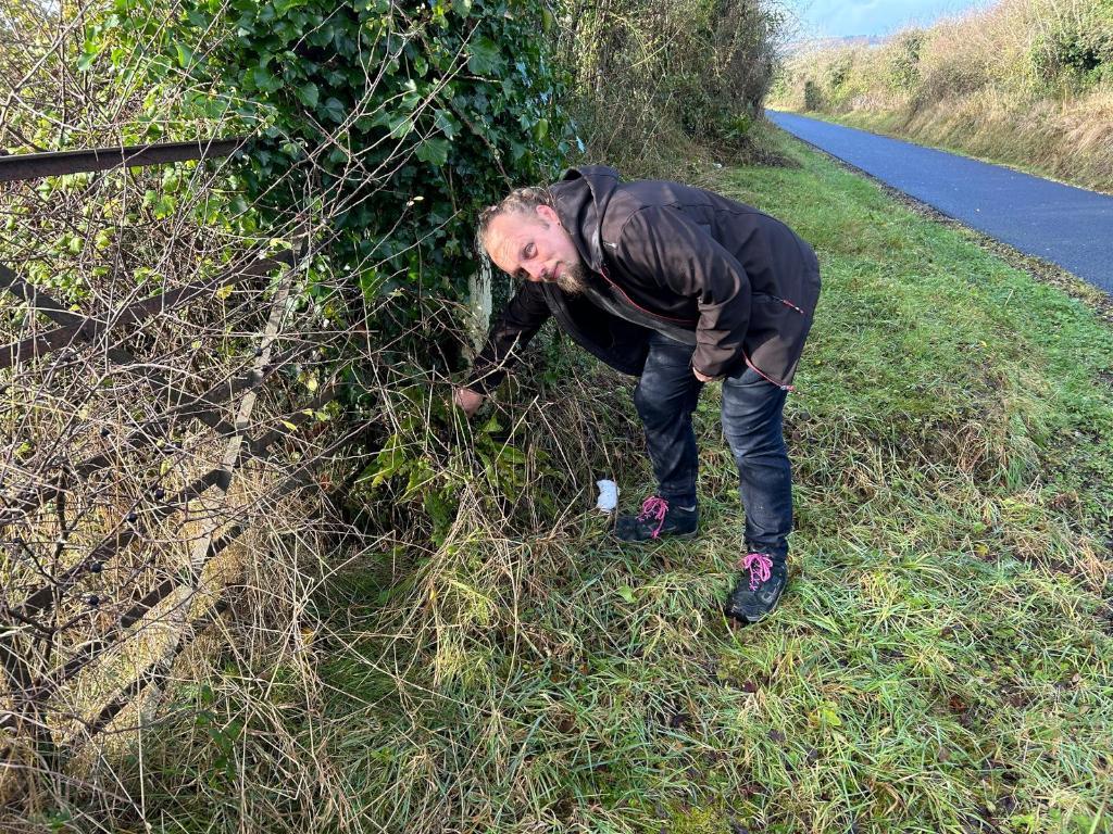 Full image of Dan reaches behind a fence post.