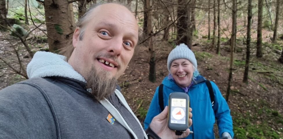Dan and his mother smile for the camera in a forest, holding a GPSr between them.