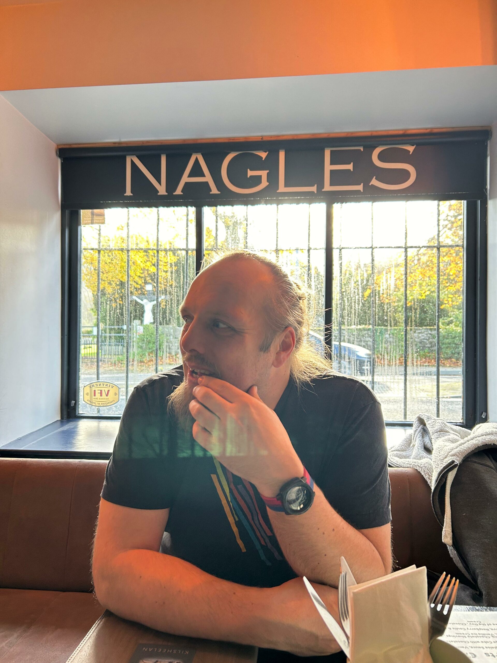 Full image of Dan sits in a bar; the word 'Nagles' is over his head on a sign.