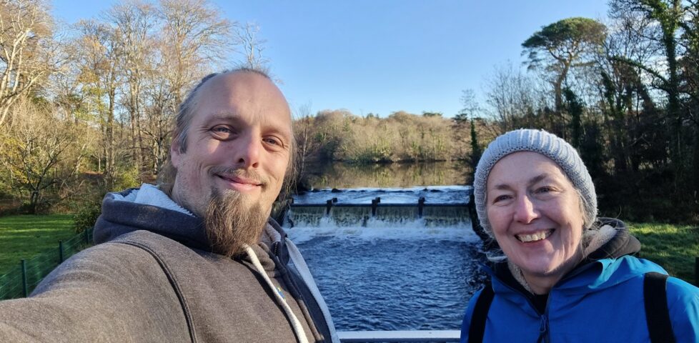Dan and his mother stand on a bridge with a weir behind them.