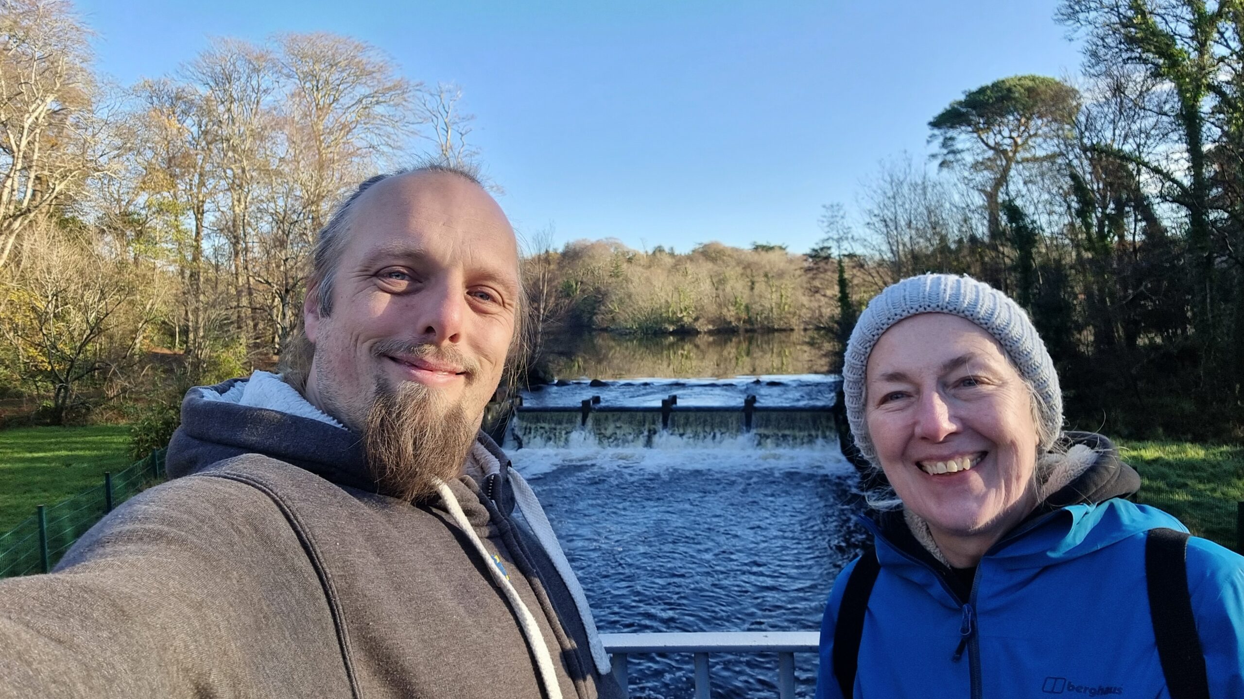 Full image of Dan and his mother stand on a bridge with a weir behind them.