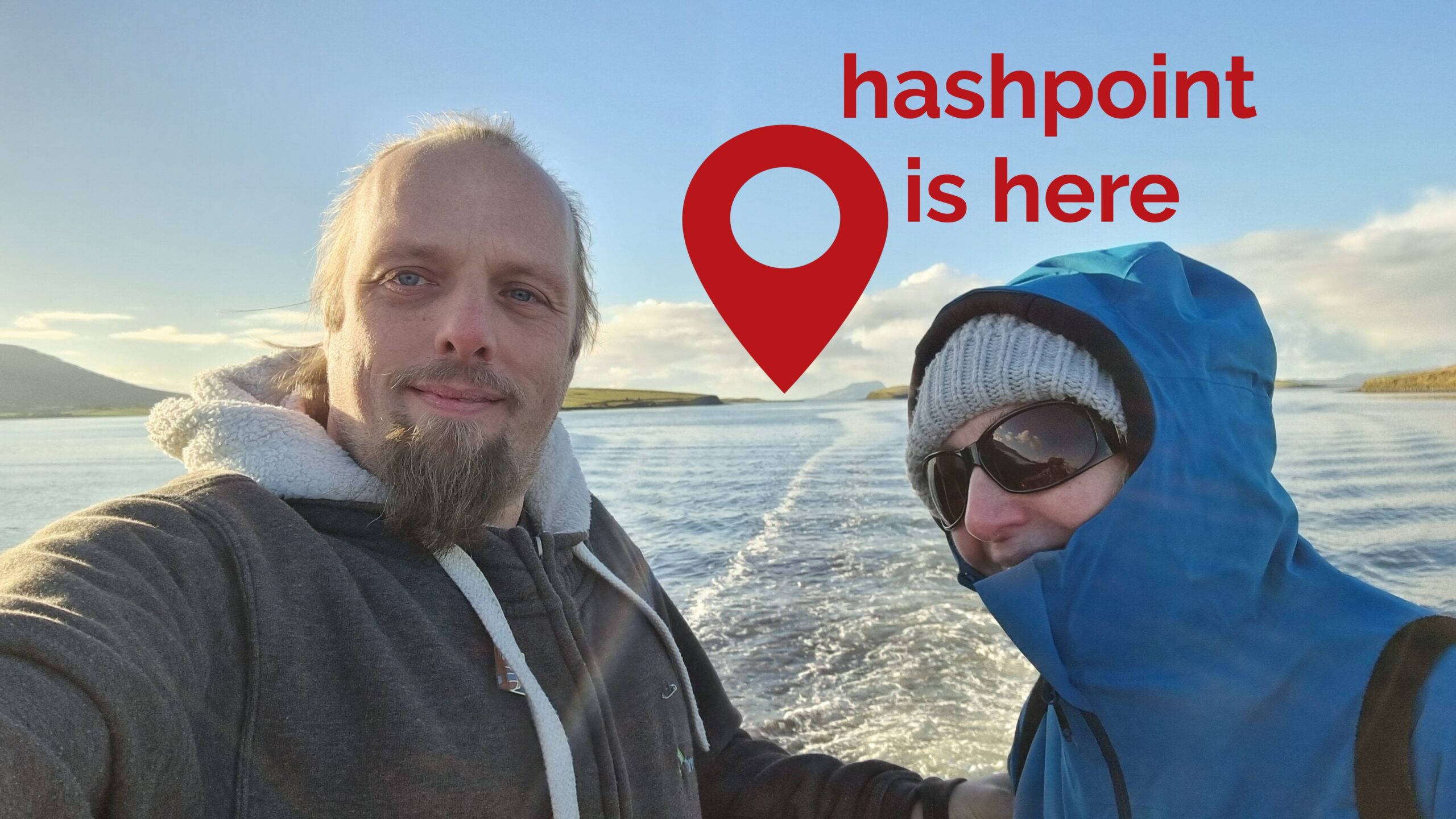 Full image of Dan and his mother ride on the back of a boat through a bay full of islands. In the distance, the distinctive shape of Clare Island can be seen, jutting out from the sea, and to the left of it a red pin is superimposed upon the image with the message 'hashpoint is here'.