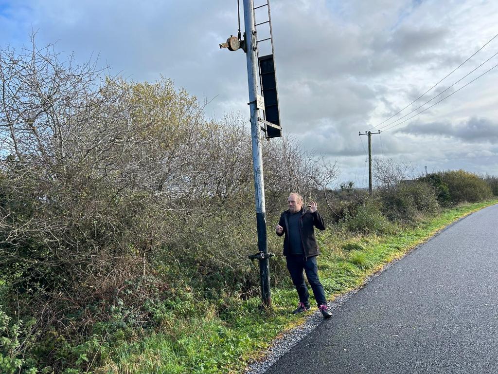 Full image of Dan stands by an old fashioned railway signal.