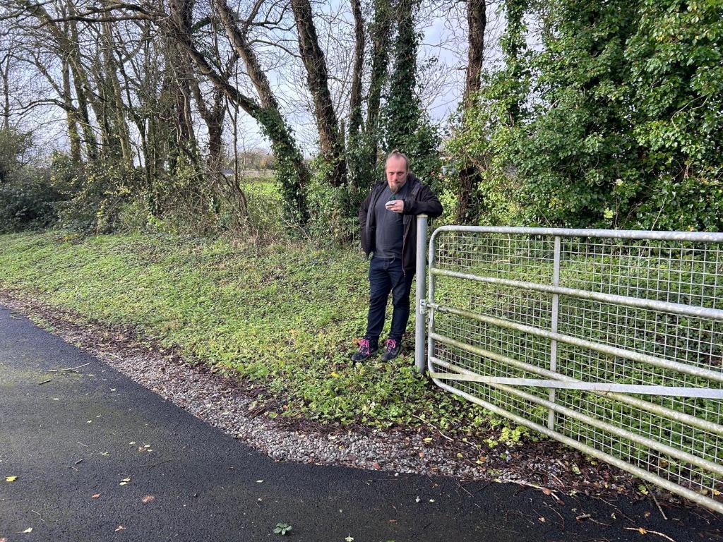 Full image of Dan leans against the post of an open metal gate.