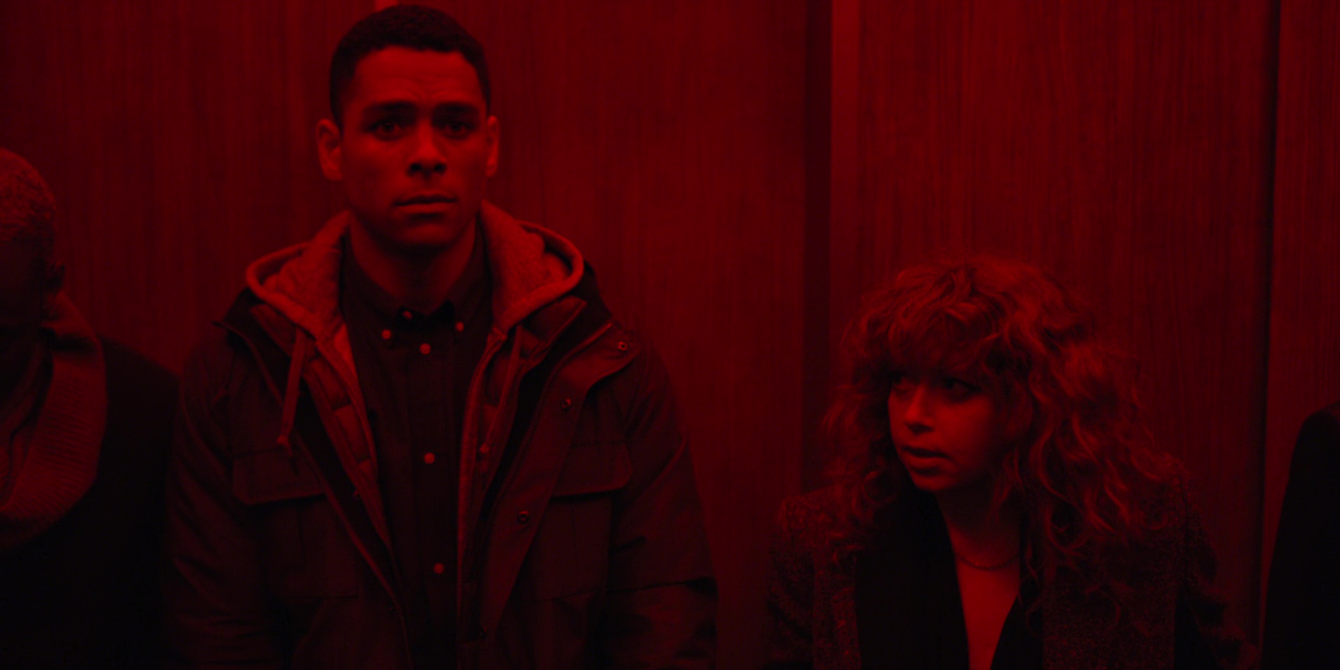 Full image of Screengrab from the third episode of Russian Doll, showing Alan (Charlie Barnett) and Nadia (Natasha Lyonne) standing in a lift whose red emergency lights have come on.