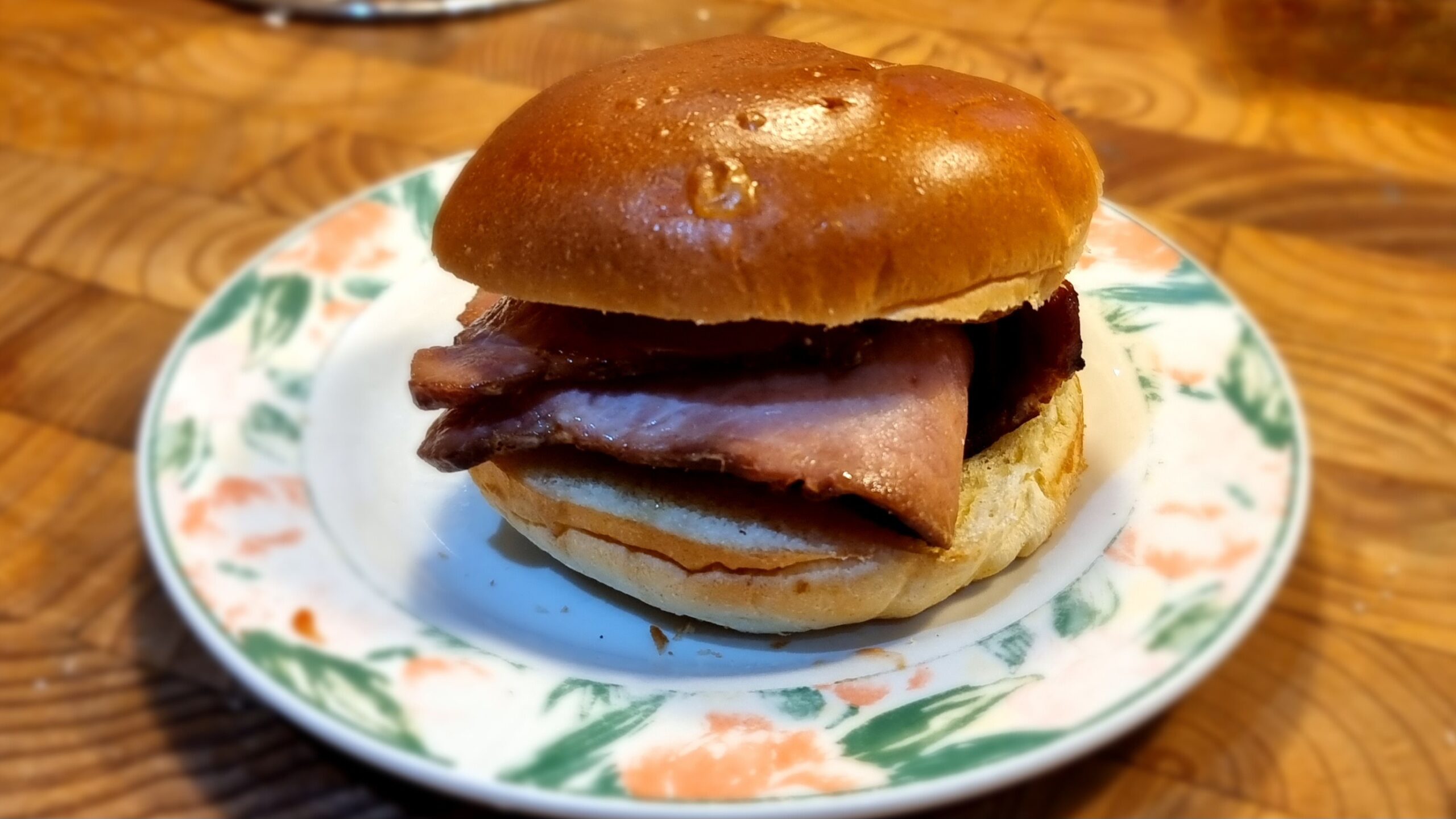 Full image of Brioche bun loaded with thick cut bacon rashers, plated, on a wooden surface.