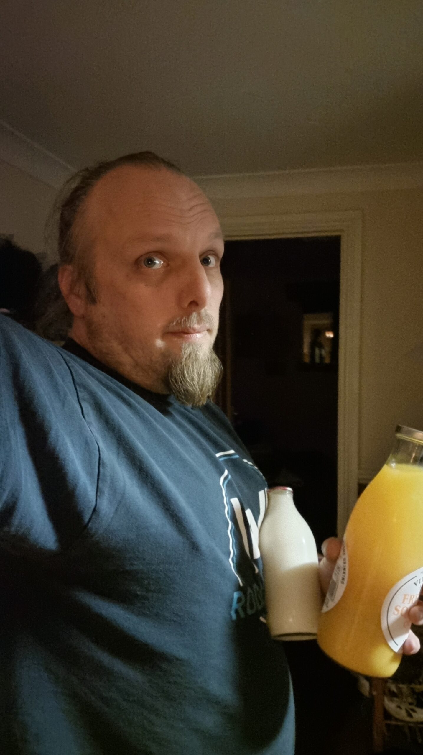 Full image of Dan,looking tired, holds glass bottles of orange juice and of milk.