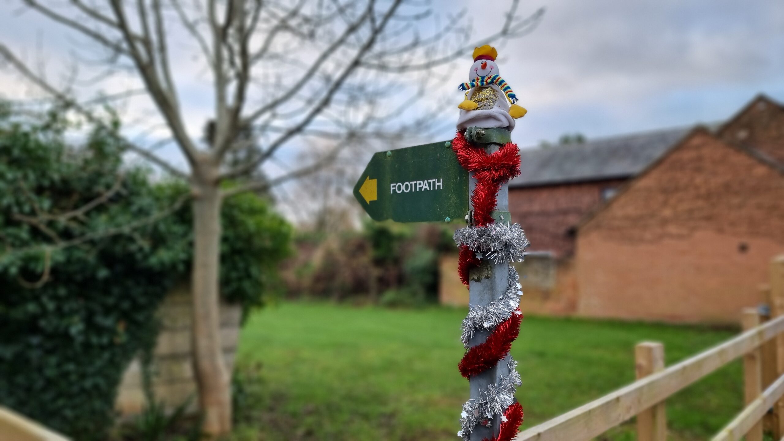 Full image of Finger post footpath sign adorned with a toy snowman and wrapped in a spiral of red and silver tinsel.