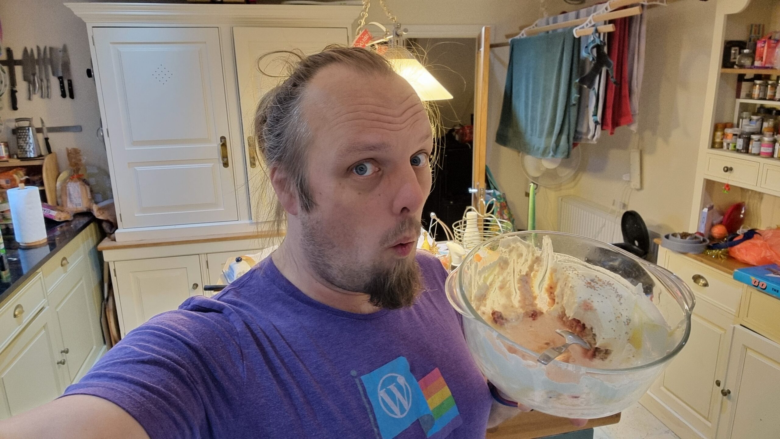 Full image of Dan, standing on a kitchen, holds a large bowl partially filled with trifle.